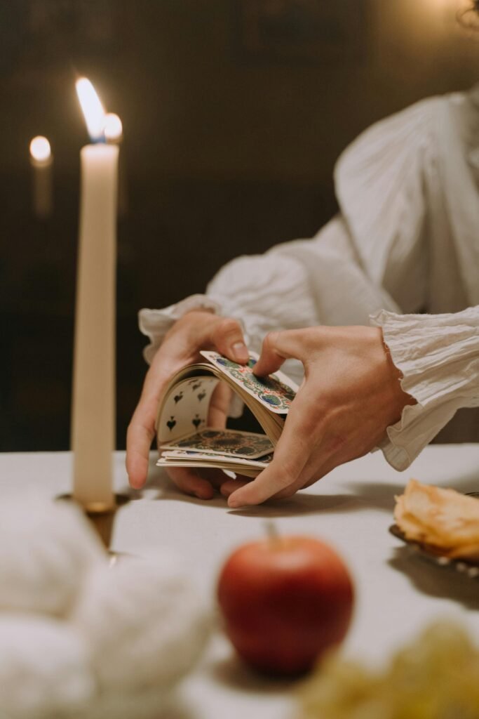 A person in historical clothing shuffles playing cards by candlelight, creating a vintage and moody atmosphere.