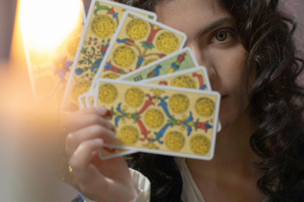 A woman with curly hair and beautiful eyes holding tarot cards, illuminated by candlelight.